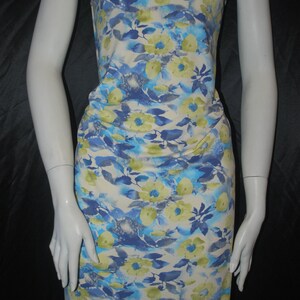 May include: White fabric with a blue and yellow floral print. The fabric has a watercolor effect and features a variety of flower shapes and sizes.
