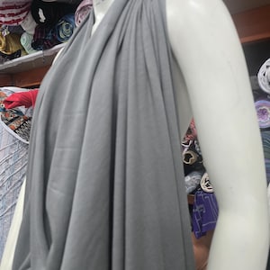 Op de afbeelding: Een effen grijze stof gedrapeerd over een witte etalagepop-torso. De stof heeft een gladde, matte textuur en is geplooid bij de halslijn, waardoor verticale plooien ontstaan die naar beneden vallen. De nek van de etalagepop toont een klein Priority Mail-label.