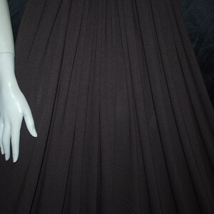 May include: A brown pleated skirt with a white mannequin arm extending from the left side of the image.