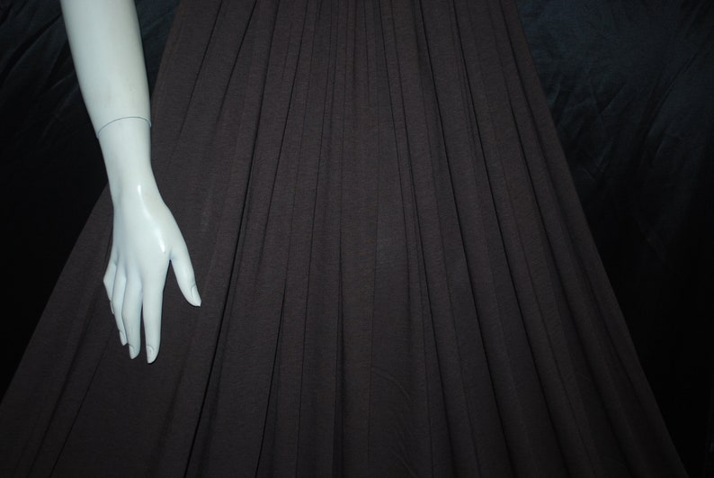 May include: A brown pleated skirt with a white mannequin arm extending from the left side of the image.