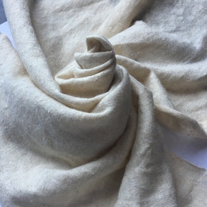 Peut inclure: Une &eacute;charpe cr&egrave;me, tiss&eacute;e l&acirc;chement, est drap&eacute;e et enroul&eacute;e avec art, cr&eacute;ant une apparence douce et textur&eacute;e. Le tissu a une surface l&eacute;g&egrave;rement in&eacute;gale, sugg&eacute;rant une fibre naturelle. Les plis et les courbes de l'&eacute;charpe ajoutent de la profondeur et de l'int&eacute;r&ecirc;t visuel.