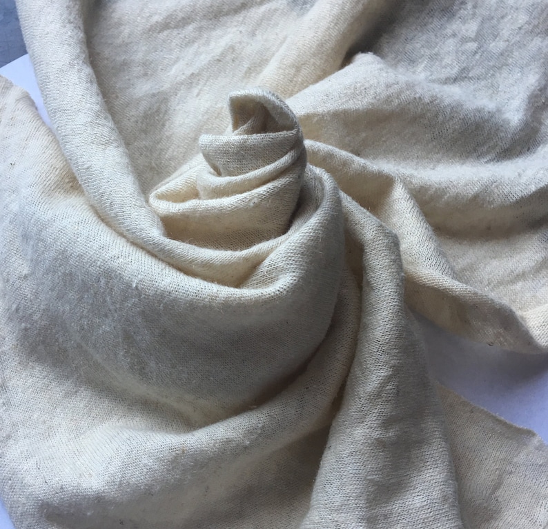 Peut inclure: Une &eacute;charpe cr&egrave;me, tiss&eacute;e l&acirc;chement, est drap&eacute;e et enroul&eacute;e avec art, cr&eacute;ant une apparence douce et textur&eacute;e. Le tissu a une surface l&eacute;g&egrave;rement in&eacute;gale, sugg&eacute;rant une fibre naturelle. Les plis et les courbes de l'&eacute;charpe ajoutent de la profondeur et de l'int&eacute;r&ecirc;t visuel.