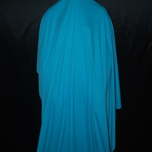 May include: A person is completely covered in a bright turquoise blue fabric. The fabric is draped over the person's head and body, creating a mysterious and shadowy silhouette.