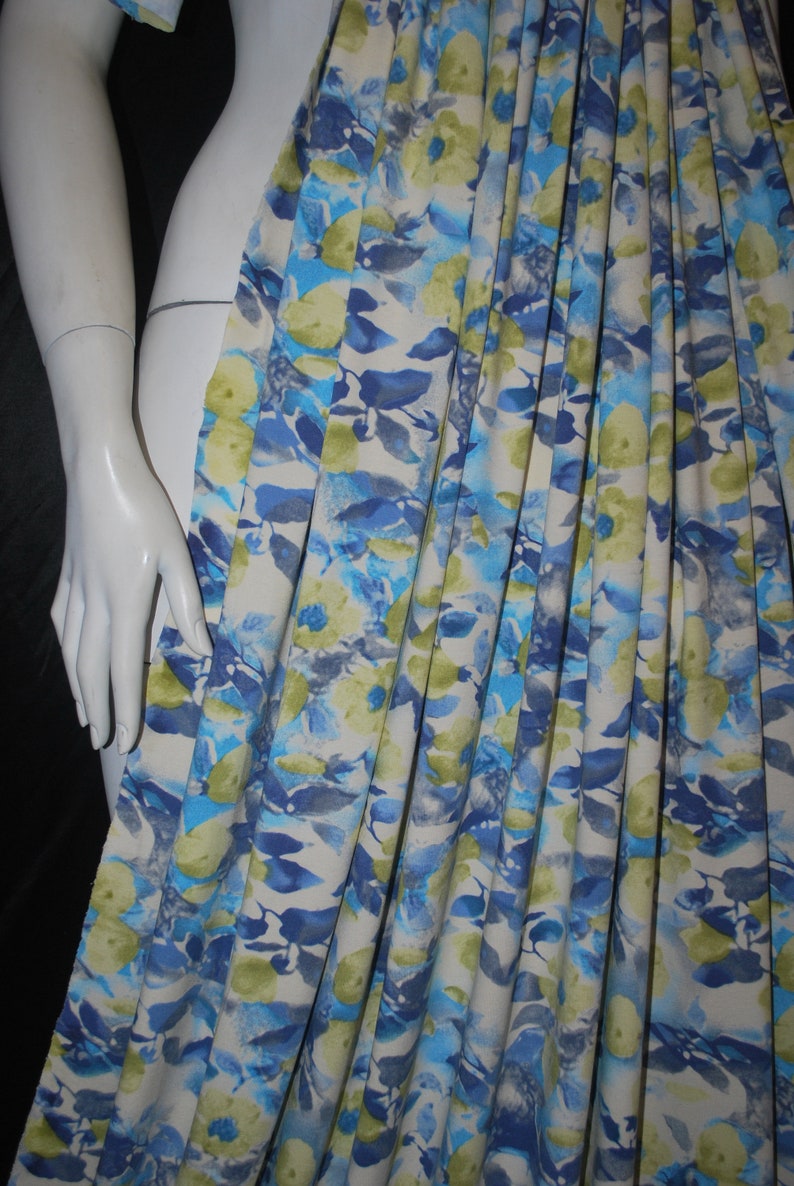 May include: A white fabric with a blue and green floral print. The fabric is pleated and has a soft, watercolor-like design.