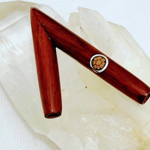 Puede incluir: Un bolígrafo de madera hecho a mano con un rico acabado marrón rojizo. El bolígrafo presenta una banda decorativa plateada con un diseño floral. La tapa del bolígrafo está separada, revelando la punta. El bolígrafo se muestra sobre una superficie cristalina blanca.