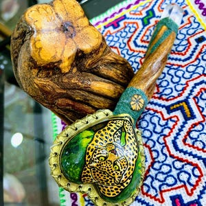 May include: A handcrafted wooden pipe with a carved leopard design on the bowl. The pipe features a gold-coloured rim, green accents, and a clear crystal at the end. The stem is made of wood and green material.