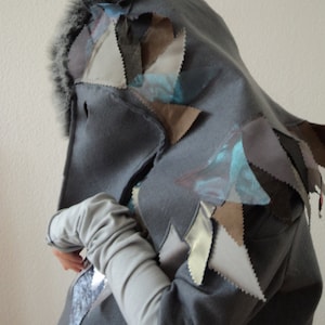 May include: A gray hooded sweatshirt with a patchwork design of various colored fabric triangles. The hood has a gray fur trim.