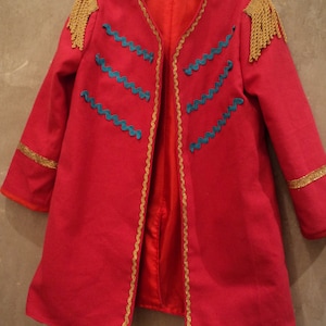 May include: A red jacket with gold trim and blue accents. The jacket has a stand-up collar and long sleeves.