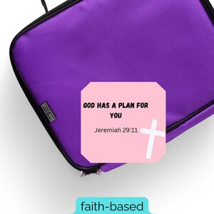 May include: A purple lunchbox with a black handle and zipper. A pink card with the text "GOD HAS A PLAN FOR YOU" and "Jeremiah 29:11" is on the lunchbox. A white cross is next to the text. The words "faith-based lunchbox cards" are below.