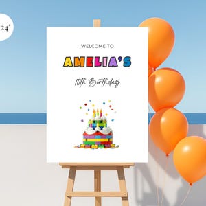 Könnte beinhalten: Ein weißes Schild auf einer hölzernen Staffelei mit dem Text "WELCOME TO AMELIA'S 10th BIRTHDAY". Das Schild zeigt einen bunten Kuchen aus Spielzeugblöcken und wird von orangefarbenen Luftballons begleitet.
