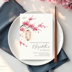 May include: A white invitation card with a floral design and the text "Hibachi Party" and "Please join us to celebrate Elizabeth's 50th Birthday". The card is on a white plate with chopsticks and a blue napkin. Pink cherry blossoms are in the background.