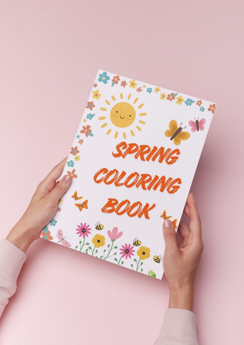 May include: A white coloring book titled "Spring Coloring Book" held against a pink background. The cover features a smiling sun, butterflies, flowers, and bees. The title is in orange, with a floral border.