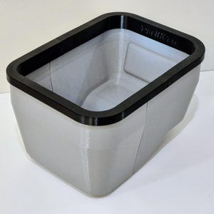 May include: A rectangular, light gray container with a black rim. The container has a slightly textured surface and the text "PediCan" is visible on the rim. The design is modern and minimalist.