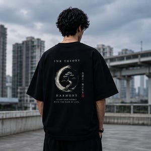 May include: A black short-sleeve t-shirt featuring a white circular brushstroke graphic with a bonsai tree inside. The text reads INK THEORY, HARMONY, ALIGN YOUR ENERGY WITH THE FLOW OF LIFE, and Japanese characters with a small red square stamp.