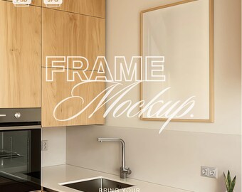 Op de afbeelding: Een keukeninterieur met licht houten kasten, een roestvrijstalen kraan en een ingelijste mockup aan de muur. De tekst "FRAME Mockup" staat over de afbeelding, samen met de zin "BRING YOUR DESIGNS TO LIFE."