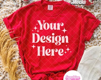 May include: A red t-shirt with the text "Your Design Here" in white, with star accents. The shirt is displayed with a white cowboy boot, disco balls, and decorative wheat on a leopard print blanket.