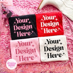 May include: Four folded t-shirts in black, red, pink, and white, each with the text "Your Design Here" in a contrasting color. The shirts are arranged on a pink leopard print surface.