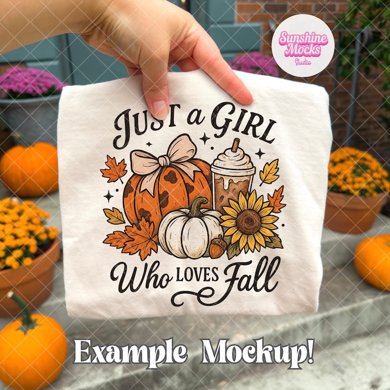 Puede incluir: Una camiseta blanca con el texto "Just a Girl Who Loves Fall" y un dise&ntilde;o de calabaza, bebida de caf&eacute;, girasol y hojas. La camiseta est&aacute; sostenida por una mano, con calabazas y flores en el fondo.
