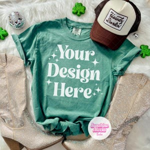 May include: A green t-shirt with the text "Your Design Here" in white, paired with a brown and cream trucker hat that says "Howdy Darlin'". The image also features rhinestone-studded boots and decorative shamrocks.