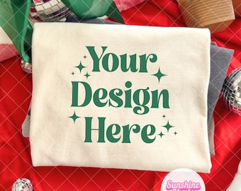 May include: A cream-colored t-shirt with the text "Your Design Here" in green, surrounded by stars. The shirt is on a red patterned surface, with white boots, disco balls, and green ribbon in the background.