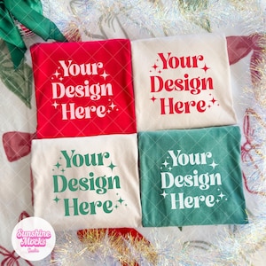 May include: Four t-shirts in red, cream, and teal green, each with the text "Your Design Here" in a retro font. The shirts are arranged on a festive background with holiday decorations. The Sunshine Mocks Studio logo is in the bottom left corner.
