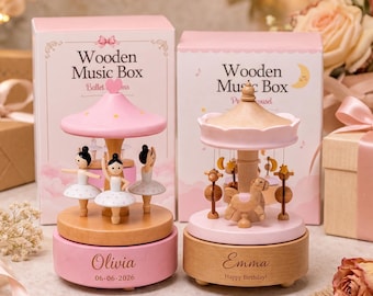 May include: Two wooden music boxes with pink and natural wood finishes. The left box features three ballerinas and the name Olivia with the date 06-06-2026. The right box features carousel horses and the name Emma with the text Happy Birthday.
