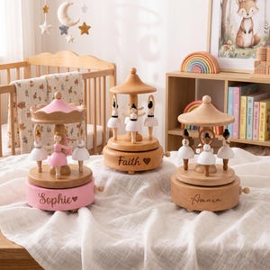 May include: Three wooden musical carousel toys featuring rotating ballerina figures. The left carousel is pink with the name Sophie, the center is natural wood with the name Faith, and the right is natural wood with the name Amara, each with a heart.
