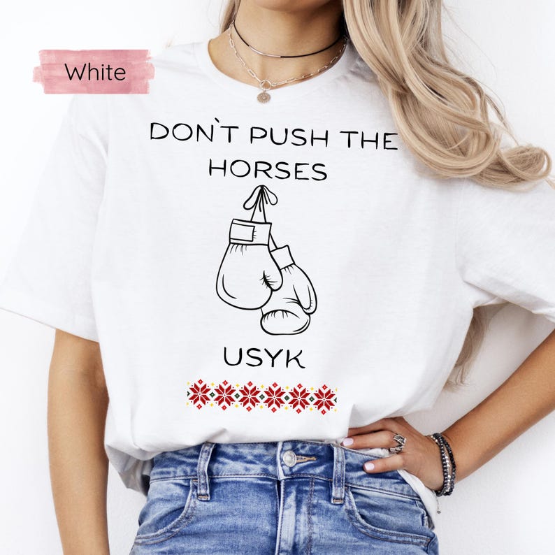 May include: White t-shirt with the text "DON'T PUSH THE HORSES" above a graphic of boxing gloves. The word "USYK" is below the gloves, with a red and white floral pattern at the bottom. The word "White" is in a pink box in the upper left.