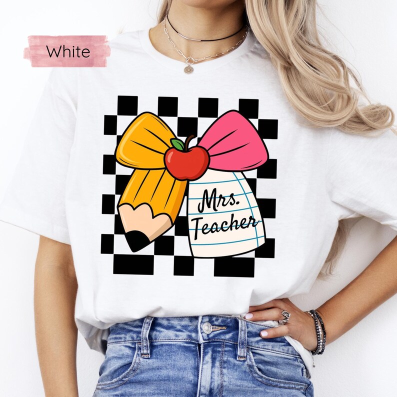 Puede incluir: Camiseta blanca con un dise&ntilde;o tem&aacute;tico para profesores. El dise&ntilde;o incluye un l&aacute;piz amarillo, un lazo rosa, una manzana roja y un bloc de notas con el texto "Mrs. Teacher" sobre un fondo a cuadros blanco y negro.