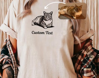 Puede incluir: Camiseta beige con una ilustración en blanco y negro de un gato y el texto "Custom Text". Una pequeña imagen de un gato está en la esquina superior derecha. La camiseta es de estilo casual.
