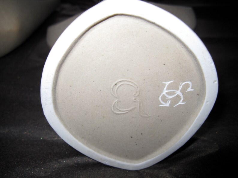 Peut inclure: Gros plan du fond d'un vase en c&eacute;ramique blanche avec une marque du fabricant qui se lit "G & S" en cursive.
