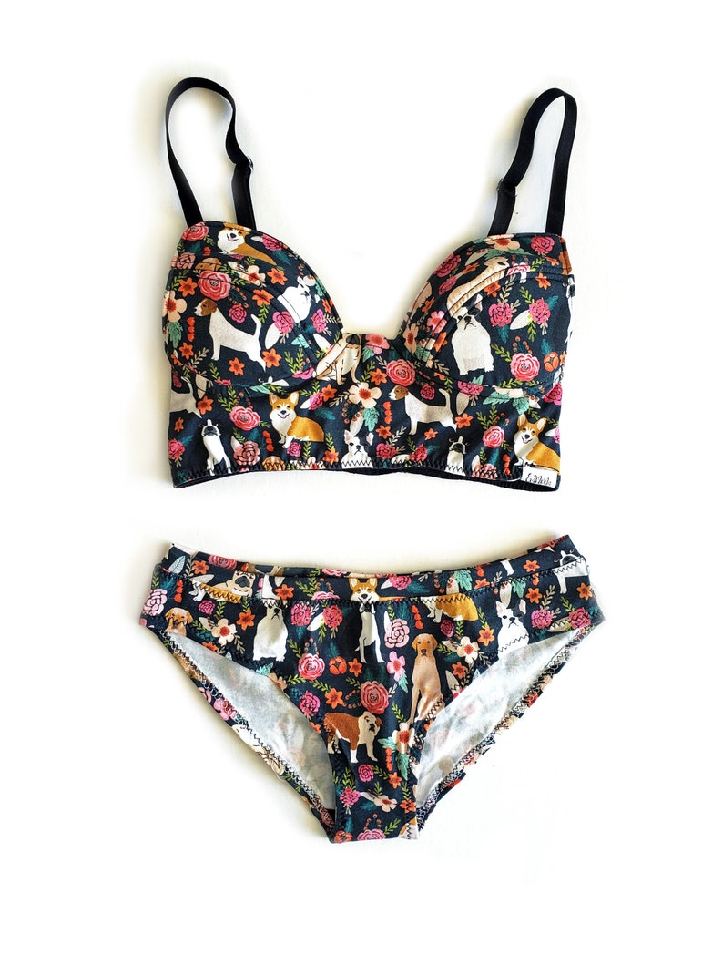 May include: Black and floral print underwear set featuring a variety of dog breeds. The bra has a push-up style and the panty is a high-cut brief.