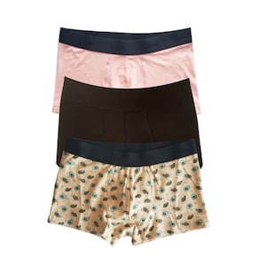 Op de afbeelding: Drie paar boxershorts. Eén paar is roze, één paar is bruin en één paar is beige met een blauwe en groene oogprint.