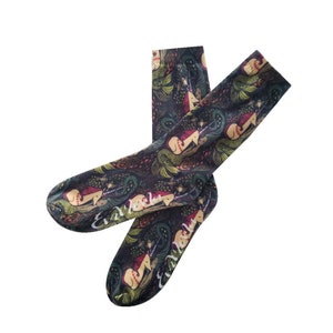 Peut inclure: Une paire de chaussettes noires avec un imprimé coloré de sirènes et de licornes. Les chaussettes portent le texte "Enchanted".