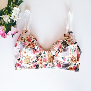 May include: A floral print bra with cats and flowers. The bra has adjustable straps and a white band.