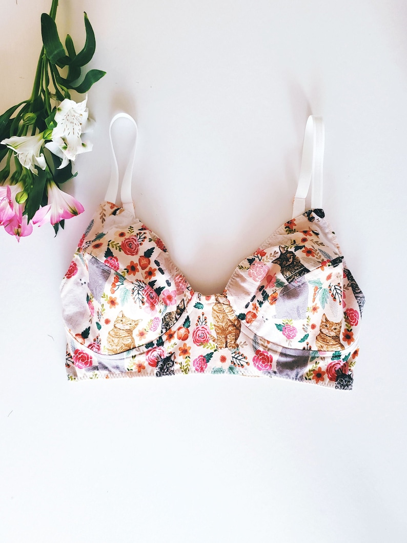 May include: A floral print bra with cats and flowers. The bra has adjustable straps and a white band.