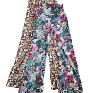 May include: Two pairs of wide-leg pants with floral prints. One pair is a dark green with pink, white, and purple flowers. The other pair is a brown with a white and pink dog print.
