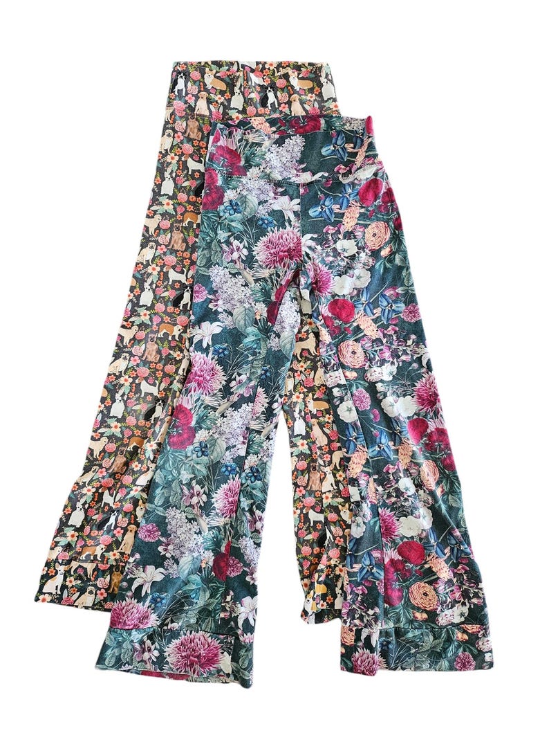 May include: Two pairs of wide-leg pants with floral prints. One pair is a dark green with pink, white, and purple flowers. The other pair is a brown with a white and pink dog print.