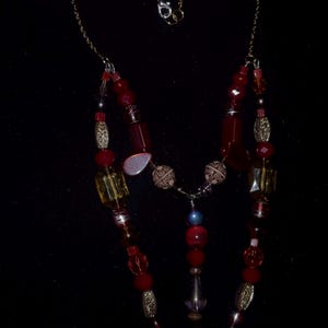 May include: A multi-strand necklace with red, yellow, and silver beads. The necklace features a variety of bead shapes and sizes. The necklace has a gold-coloured chain and clasp.