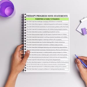 May include: A spiral-bound notebook with the title "THERAPY PROGRESS NOTE STATEMENTS" and the subtitle "PARENTING & FAMILY DYNAMICS." The notebook is open, displaying a list of statements. A hand holds the notebook, and another hand holds a blue pen.