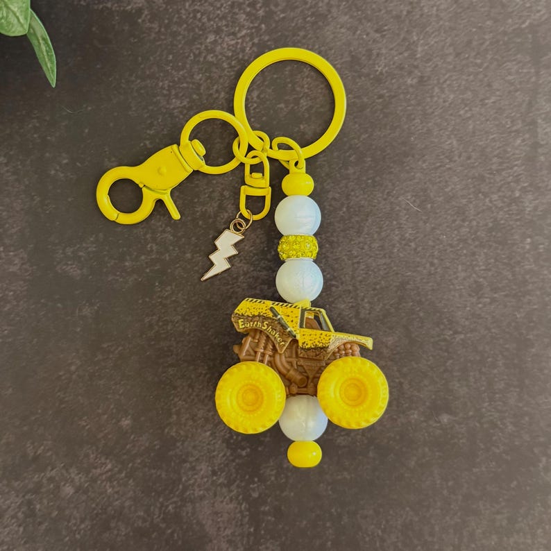 May include: Yellow monster truck keyring with a lightning bolt charm and white and yellow beads. The truck has large yellow wheels and the words "Earth Shaker". The keyring includes a clasp and a key ring.