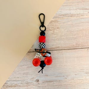 May include: A black keychain with a lobster clasp, black and red beads, and a miniature monster truck charm. The truck has red wheels and silver accents.