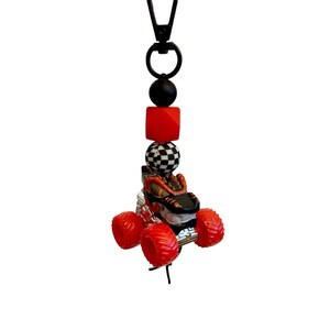 May include: A lanyard featuring a miniature monster truck charm. The charm is red, black, and silver, with large red wheels. The lanyard also includes a black clasp, black and red beads, and a checkered bead.