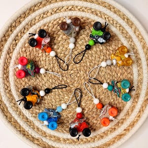 Puede incluir: Una colección de clips para chupete con camiones monstruo de juguete coloridos. Cada clip presenta un camión en miniatura con ruedas vibrantes y una cadena de cuentas. Los camiones son de varios colores, incluyendo rojo, azul, naranja y verde.