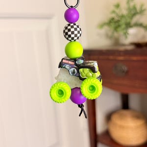 Pu&ograve; includere: Un portachiavi con un ciondolo a forma di monster truck Grave Digger, ruote verde neon e carrozzeria nera e verde. Il portachiavi include anche perline viola, a scacchi e verdi.