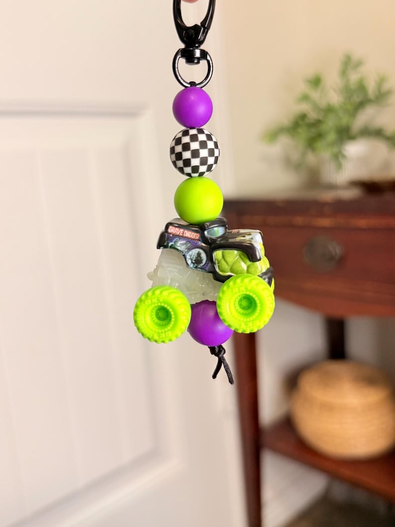 Pu&ograve; includere: Un portachiavi con un ciondolo a forma di monster truck Grave Digger, ruote verde neon e carrozzeria nera e verde. Il portachiavi include anche perline viola, a scacchi e verdi.