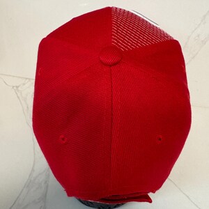 May include: A bright red baseball cap featuring a structured front panel with a fabric-covered button at the crown and a breathable white mesh back panel. The cap has a classic six-panel construction with stitched eyelets for ventilation.