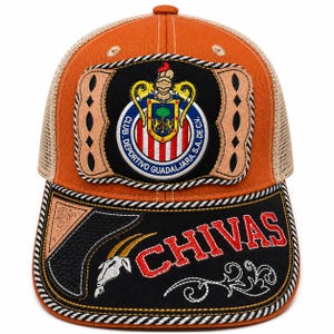 May include: An orange and tan mesh trucker hat featuring a prominent Club Deportivo Guadalajara crest on the front panel. The black brim displays the word CHIVAS in red letters, a white goat skull graphic, and decorative tan leather-like accents.