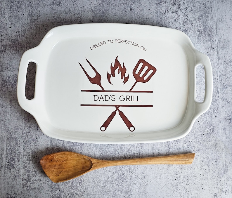 May include: White ceramic serving tray with brown handles and a brown graphic of crossed grilling tools, a flame, and the text "Grilled to perfection on Dad's Grill".