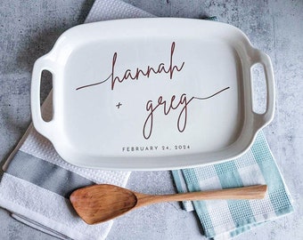 May include: White ceramic serving tray with a red cursive inscription that reads "hannah + greg" and the date "FEBRUARY 24, 2024".